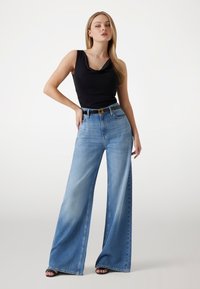 Jeans a gamba larga di colore blu chiaro con una finitura sbiadita, vita alta e cinque tasche. Abbinati a un top senza maniche nero e una cintura con fibbia dorata.