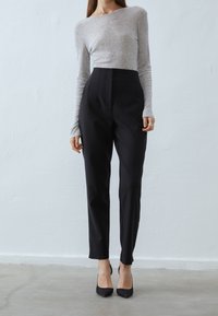 Haut gris à manches longues associé à un pantalon noir taille haute, présentant une coupe ajustée et une texture lisse. Des chaussures à talons noires complètent la tenue.