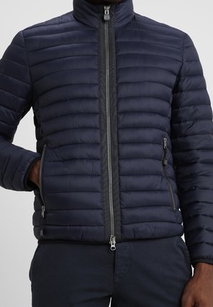Navyblaue gepolsterte Jacke mit hohem Kragen, vertikalem Nähmuster, Frontreißverschluss und zwei seitlichen Reißverschlusstaschen. Leichter Stoff.