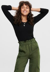 Schwarzes Langarmoberteil mit figurbetontem Schnitt, kombiniert mit olivgrünen, hoch taillierten Cargo-Hosen mit Seitentaschen und gerafftem Bund.