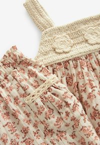 Blommönstrad bomulls klänning med beige bakgrund, rynkad livstycke och dekorativa virkade detaljer. Har justerbara spaghettiband.