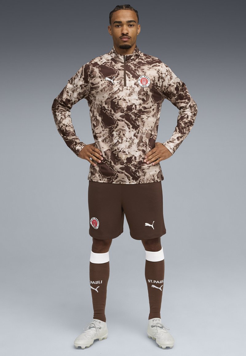 Brun og beige camouflage langærmet trøje med et hvidt logo, parret med brune shorts og sokker med hvide accenter og logo.