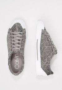 Grijze stoffen sneakers met een patroonontwerp, witte rubberen zool en contrasterende accenten. Voorzien van een ronde neus en veterluiting.