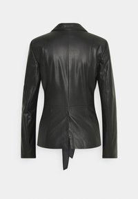 Svart läderblazer med en strukturerad design, sned krage och långa ärmar. Har en slits bak och en knutdetalj vid nederkanten.