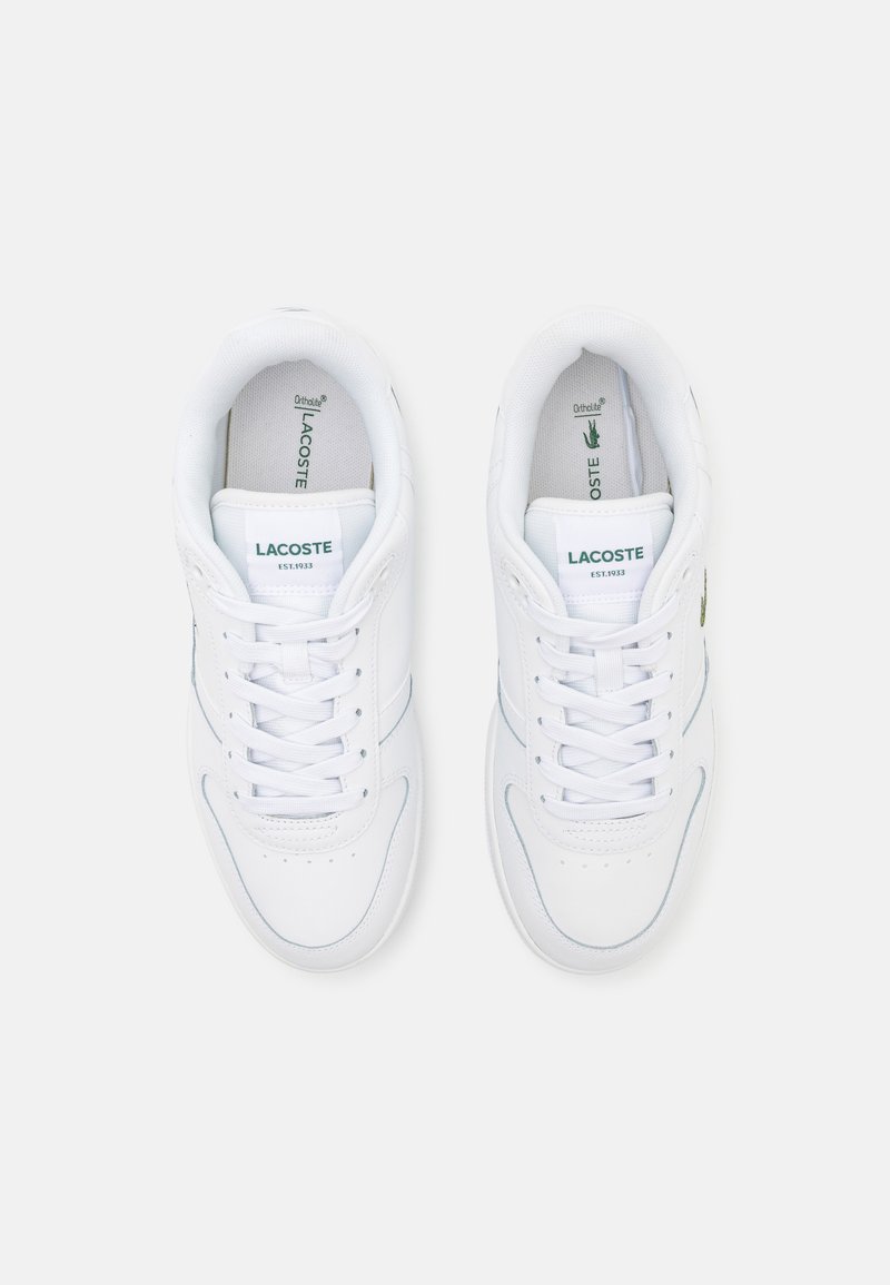 White lace-up sneakers with a smooth leather upper, green and blue accents, and lace holes. Features the Lacoste logo and cushioned insoles.