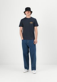 Navy blue cotton t-shirt with yellow "Florida" text, paired with loose-fitting blue denim jeans and white sneakers. Bucket hat in black.