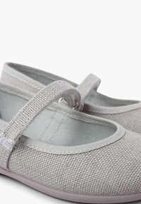 Zapatos de textil grises con un diseño plano, que cuentan con una correa en el empeine y una parte superior tejida texturizada. Forro suave y suela de goma.