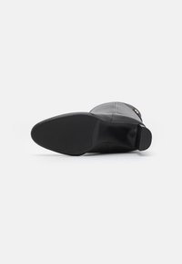 Botte noire en cuir montée jusqu'au genou avec une texture lisse, bout rond, épais talon bloc et semelle en caoutchouc neutre. Intérieur doublé.