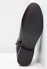 Černé kotníkové boty s hladkým koženým svrškem a texturovanou gumovou podrážkou. Obsahují prošívání a jemné logo na podrážce.