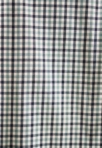 Tessuto a quadri verde e bianco con accenti neri, caratterizzato da un classico motivo a scacchi. La texture appare morbida e leggera.