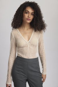 Lace long-sleeve top in cream with a V-neck and form-fitting design, paired with gray tailored trousers. Fine texture and subtle pattern.