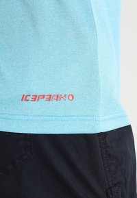 Světlomodré tričko s krátkým rukávem z měkké látky, s červeným logem "ICEPEAK" na dolní straně, v kombinaci s tmavými šortkami.