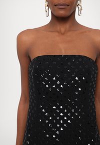 Rochie neagră fără bretele, cu un model de buline cu paiete ce au reflexii variate. Textură fină, design ajustat și culoare solidă.