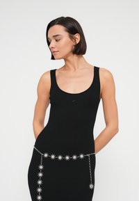 Μαύρο ριμπ φόρεμα με τιράντες και στρογγυλή λαιμόκοψη, ασημί αλυσίδα με μοτίβο αστεράκια στη μέση, εφαρμοστή σιλουέτα, λεία υφή.