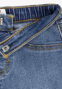 Τζιν παντελόνια με μπλε πλύσιμο, με κίτρινη ραφή, κλείσιμο με ασημένιο κουμπί και διακριτική ανάγλυφη υφή. Η μ έση είναι ελαστική.