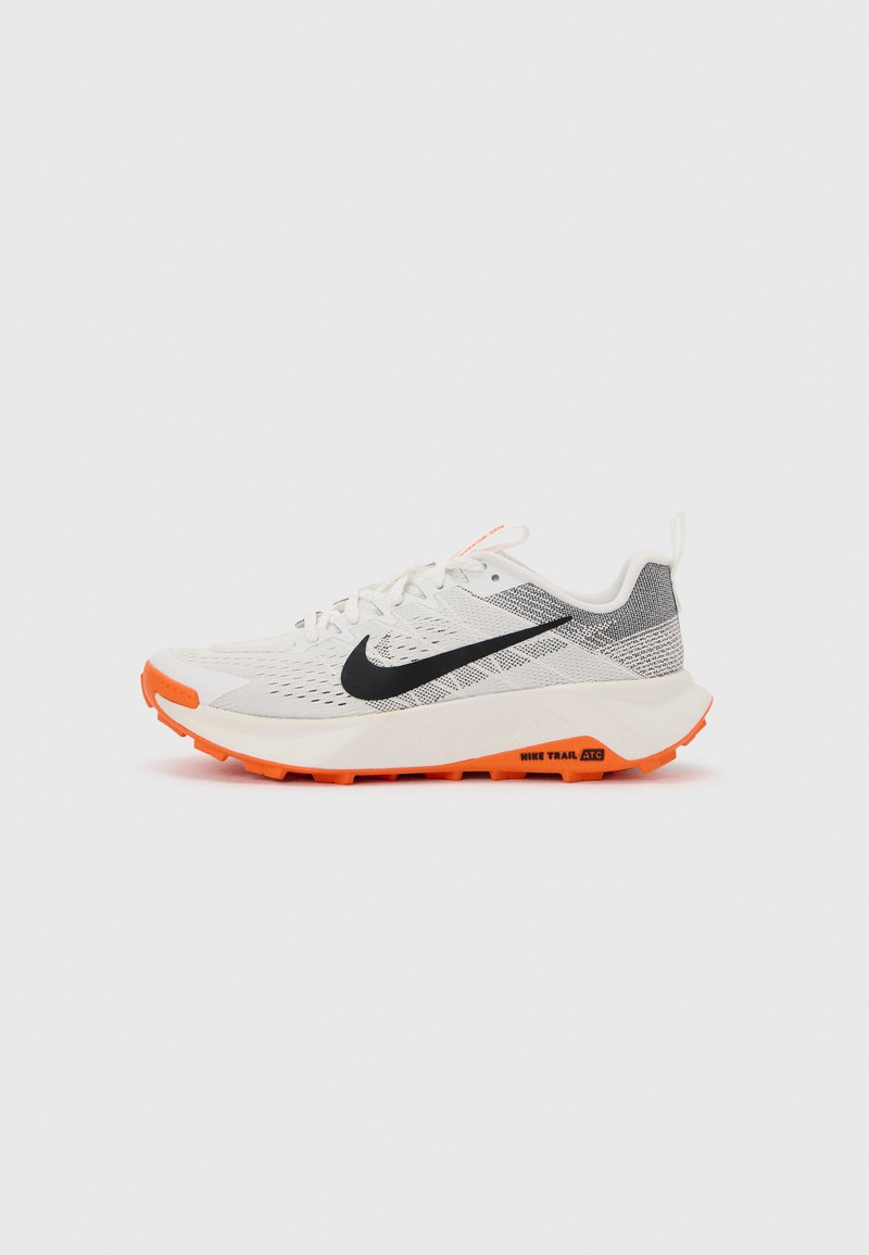 Λευκό και γκρι παπούτσι τρεξίματος Nike trail με μαύρο σήμα και πορτοκαλί σόλα, σχεδιασμένο για πρόσφυση και άνεση εκτός δρόμου.