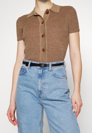 Brązowa krótka koszulka polo z prążkowanego dzianiny z guzikami, zestawiona z jasnoniebieskimi jeansami z wysokim stanem i czarnym paskiem.