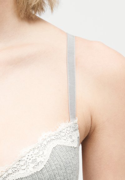 Nærbillede af en persons skulder iført en grå ribstrikket camisole med hvid blonderand og tynde justerbare stropper.
