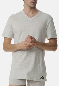 Męska szara koszulka v-neck, z krótkim rękawem, wykonana z miękkiej tkaniny, z małym czarnym logo Adidas na lewym dolnym brzegu i luźnym kroju.