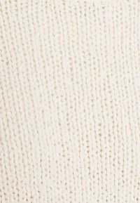 Gros plan d'un tissu tricoté de couleur crème avec une texture côtelée, fait de fil doux et épais.