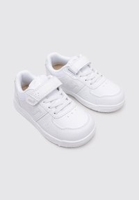 Zapatillas blancas con una textura suave de cuero, diseño con cordones, correa de velcro y un logo lateral sutil. Suela de goma con patrón antideslizante.