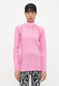 Tett langermet topp i lys rosa med geometriske mønstre, høy krage og halvglidelås foran. Kombinert med mønstrede svart-hvite tights.
