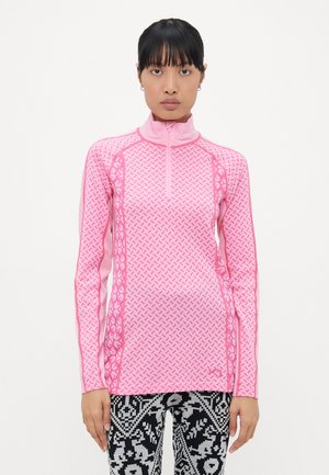 Tett langermet topp i lys rosa med geometriske mønstre, høy krage og halvglidelås foran. Kombinert med mønstrede svart-hvite tights.