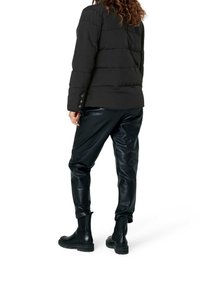 Svart vadderad jacka med distinkta horisontella sömmar, kombinerad med blanka svarta läderbyxor och kraftiga svarta ankelstövlar.