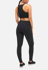 Sostén deportivo negro y leggings de cintura alta hechos de tela elástica. El conjunto presenta un diseño elegante con una textura suave, ideal para entrenamientos.