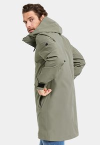 Olivgrüner Parka mit Kapuze, langes Design, Seitentaschen, verstellbare Bündchen und glattes, wasserabweisendes Material.