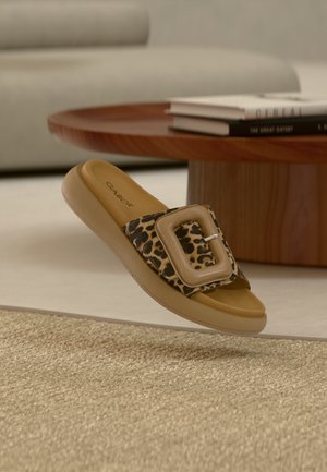 Leopardmuster-Pantoletten mit einer großen beigen Schnalle, brauner Sohle, glatter Textur und flachem Design, auf einem neutralen gewebten Teppich platziert.