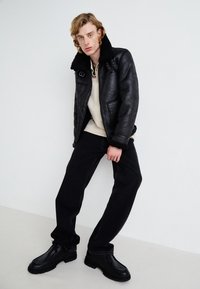 Black leather jacket with shearling collar, cream sweater, black jeans, and black lace-up shoes. Smooth texture, classic design, contrasting materials.