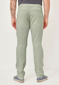 Hellgrüne Hose aus einem weichen Stoff mit strukturierter Oberfläche. Verfügt über zwei Gesäßtaschen und ein gerades Bein-Design. Getragen mit flachen Schuhen.