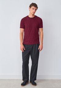 Burgundy patterned short-sleeve shirt with round neckline, paired with black loose-fit trousers and black sneakers. Minimalist design, smooth texture.