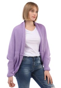 Lavenderfarbener Strickcardigan mit geripptem Muster, offener Vorderseite und langen Ärmeln. Getragen über einem weißen T-Shirt und kombiniert mit blauen Jeans.