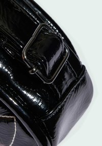 Rogata czarna z lakierowanej skóry z błyszczącym wykończeniem, wyposażona w srebrne metalowe akcesoria, detal w postaci klamry oraz teksturowane wzory na powierzchni.