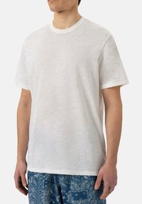 T-shirt bianca in cotone con scollatura rotonda, maniche corte e vestibilità rilassata. Tessuto leggero e design semplice, abbinato a pantaloni corti blu con motivo.