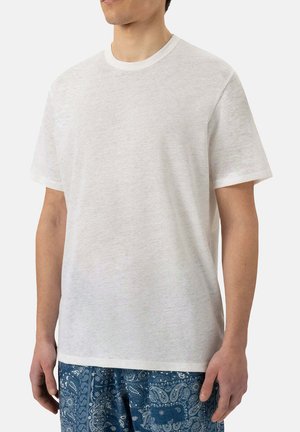 T-shirt bianca in cotone con scollatura rotonda, maniche corte e vestibilità rilassata. Tessuto leggero e design semplice, abbinato a pantaloni corti blu con motivo.