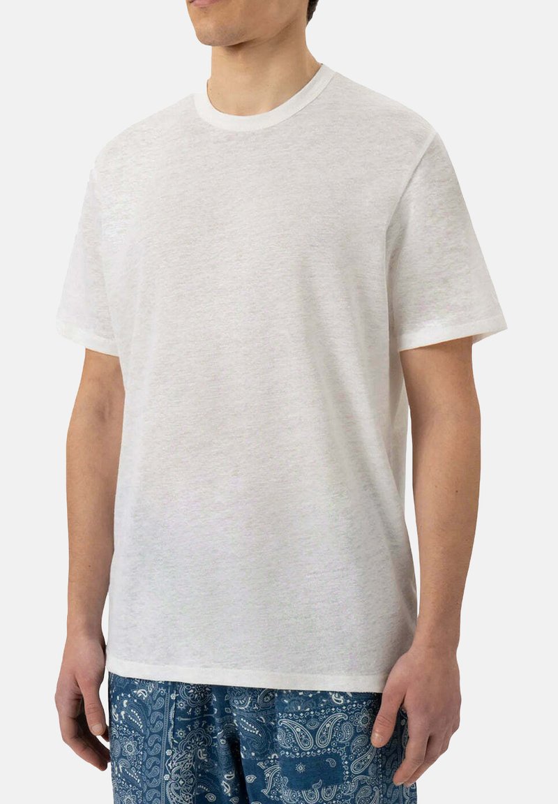 T-shirt bianca in cotone con scollatura rotonda, maniche corte e vestibilità rilassata. Tessuto leggero e design semplice, abbinato a pantaloni corti blu con motivo.
