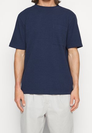 Dunkelblaues T-Shirt mit kurzen Ärmeln aus strukturiertem Stoff, ausgestattet mit einer Brusttasche und einem runden Ausschnitt in geradem Schnitt.