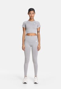 Jasnoszary zestaw odzieży sportowej, w skład którego wchodzi krótki t-shirt oraz legginsy z wysokim stanem. Materiał jest gładki, z subtelnym logo na piersi.