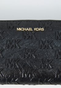 Portefeuille en cuir noir texturé présentant un motif de logo en relief, avec une inscription dorée "MICHAEL KORS" sur le devant.