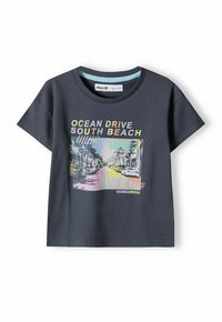 Tumši pelēks kokvilnas T-krekls ar īsām piedurknēm, uz kura attēlots krāsains grafiskais attēls ar ielas skatu, kas apzīmēts ar "OCEAN DRIVE SOUTH BEACH."