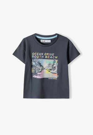 Tmavohnedé tričko z bavlny s krátkymi rukávmi, na ktorom je farebná grafika ulice s názvom "OCEAN DRIVE SOUTH BEACH."