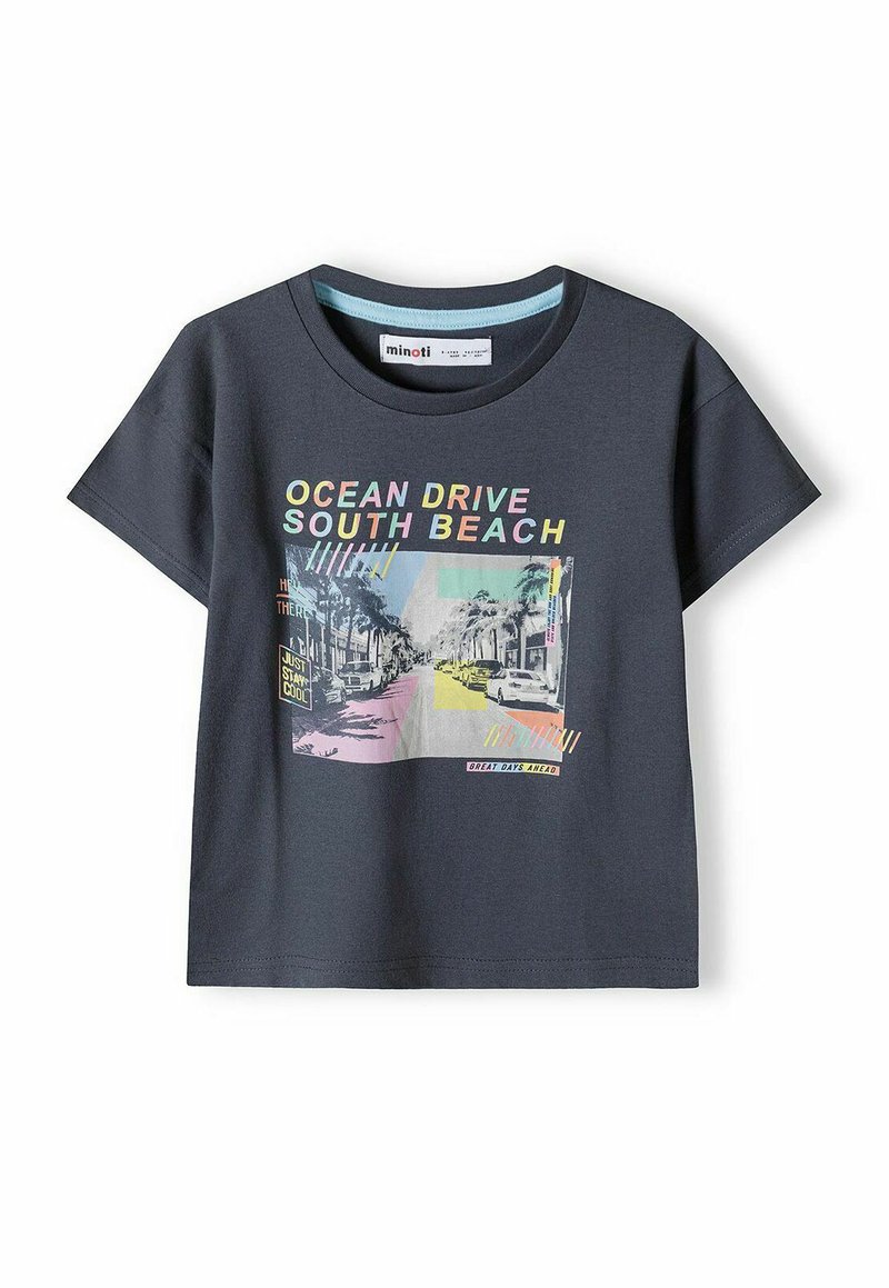 Tumši pelēks kokvilnas T-krekls ar īsām piedurknēm, uz kura attēlots krāsains grafiskais attēls ar ielas skatu, kas apzīmēts ar "OCEAN DRIVE SOUTH BEACH."