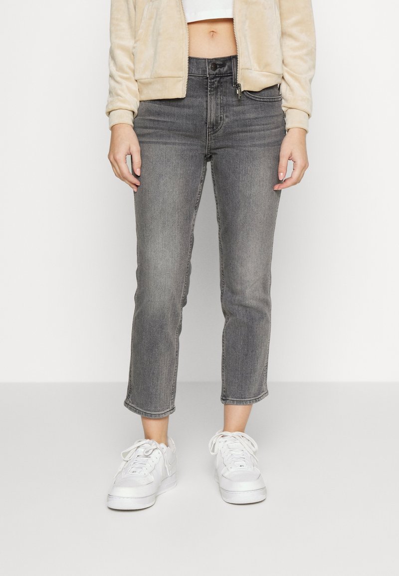 Jeans en denim gris avec une coupe droite, longueur raccourcie, design à cinq poches, associés à des baskets blanches et une veste zippée beige.