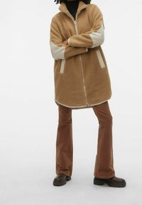 Giacca in pile marrone con collo alto e chiusura a zip, dettagli a pannello crema e due tasche laterali; abbinata a pantaloni in corduroy marroni a palazzo.