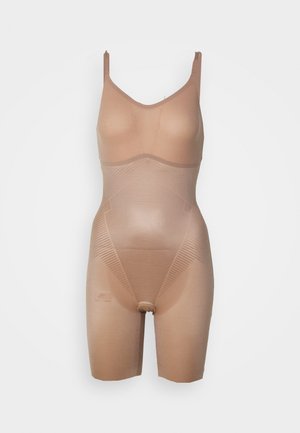 Beige shapewear bodysuit met verstelbare schouderbanden, naadloos ontwerp en textuurgedeelten voor vormgeving. Mid-thigh lengte.