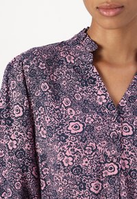 Blusa strutturata con motivo floreale che presenta uno sfondo blu navy con fiori rosa, colletto alla mandarino e dettagli con abbottonatura.
