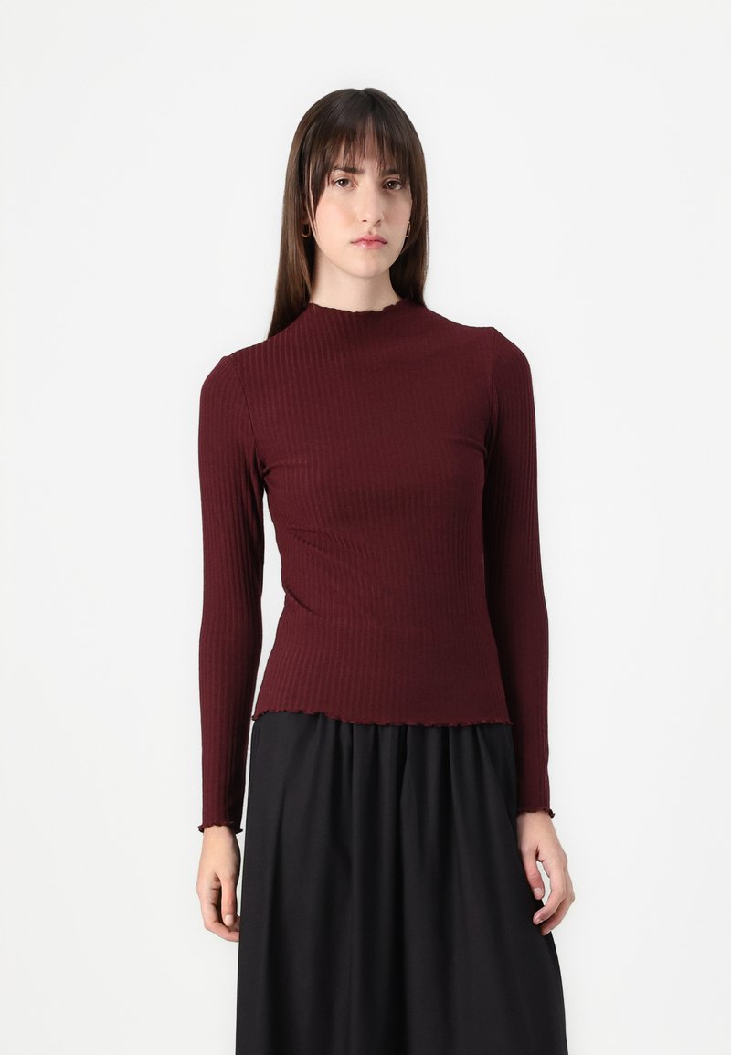 Långärmad ribbad topp i mörk burgundy med hög halsringning och rå kant, i kombination med en svart kjol för en lager-på-lager look.